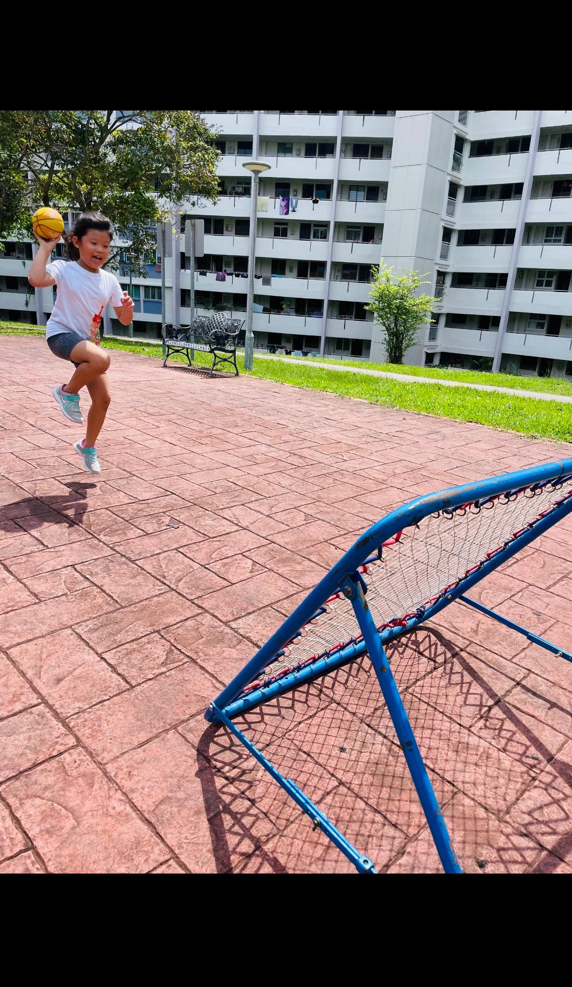 Child jumping to score a goal with a ball near a playground